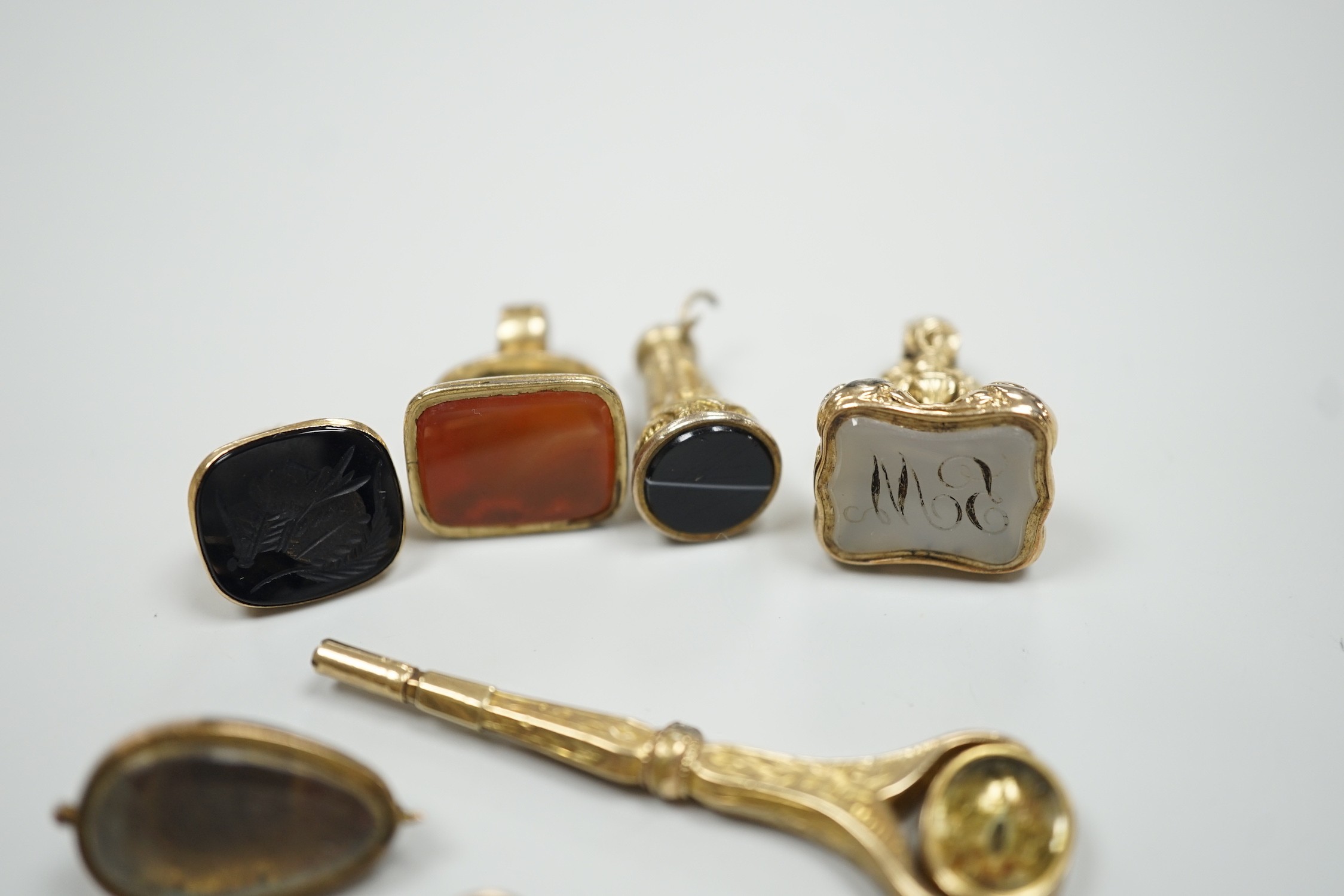 Four assorted 19th century and later yellow metal overlaid and gem set fob seals, a Victorian 15ct gold and sardonyx spinning fob, a sardonyx set locket, damaged pendant and yellow metal and two stone set watch key.